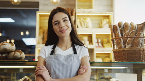 Portrait-of-the-pretty-female-bakery-vendor-standing-at-the-counter-and-smiling-to-the-camera.-Close-up.-Inside